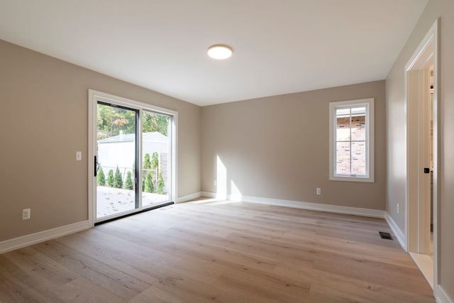 spare room featuring light wood finished floors, visible vents, and baseboards