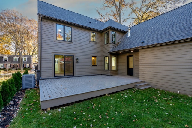 back of property featuring a wooden deck, a lawn, central AC, and roof with shingles