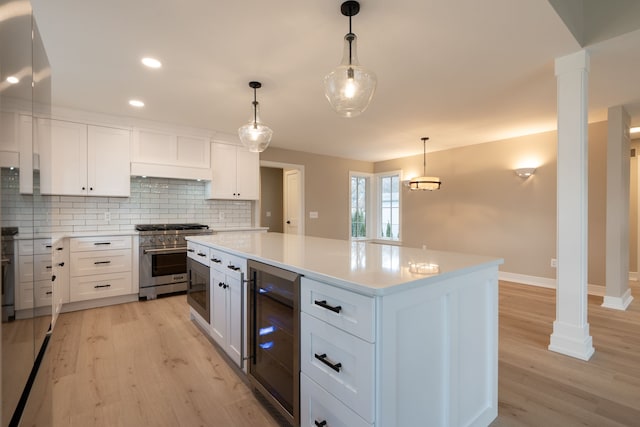 kitchen featuring stainless steel stove, wine cooler, decorative columns, and light countertops