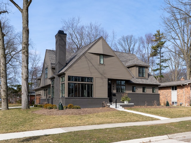 view of front facade with brick siding, a chimney, and a front yard