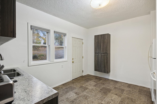 interior space featuring dark brown cabinets, sink, white fridge, and a textured ceiling