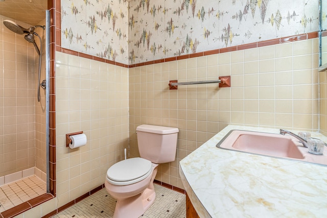 bathroom with tile patterned floors, tiled shower, toilet, vanity, and tile walls