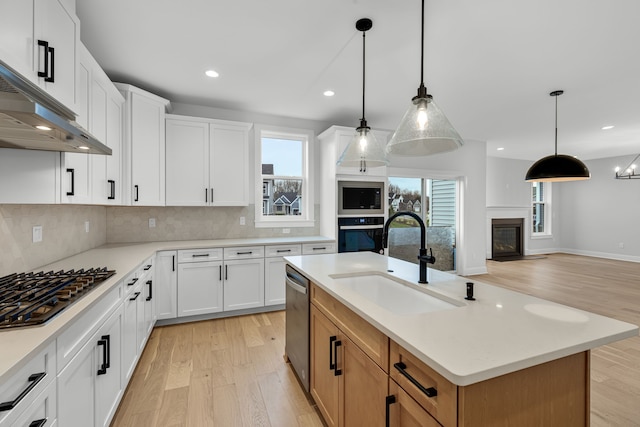 kitchen featuring appliances with stainless steel finishes, a kitchen island with sink, sink, white cabinetry, and hanging light fixtures