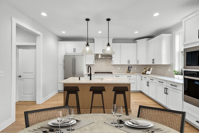 kitchen with sink, hanging light fixtures, a kitchen island with sink, white cabinets, and appliances with stainless steel finishes