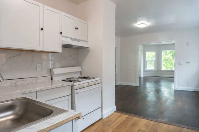 kitchen featuring white range with gas stovetop, light wood-type flooring, tasteful backsplash, and white cabinetry