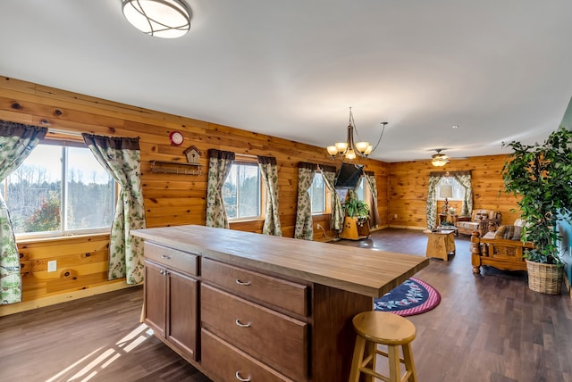 kitchen with a center island, wooden counters, ceiling fan with notable chandelier, wooden walls, and dark hardwood / wood-style flooring