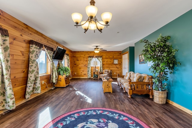 living room featuring ceiling fan with notable chandelier, dark wood-type flooring, and wooden walls