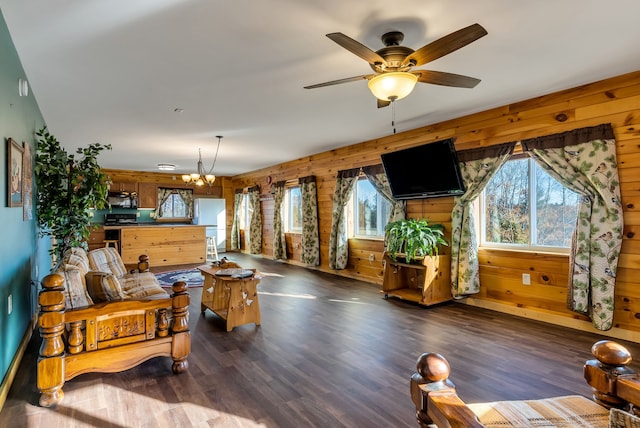 living room with wood walls, dark wood-type flooring, and ceiling fan with notable chandelier