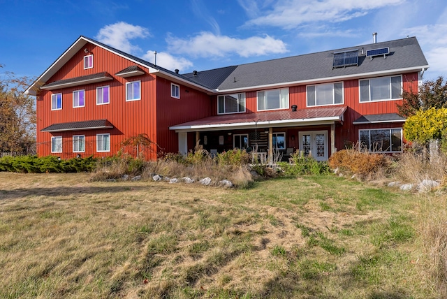 rear view of property with a lawn and solar panels