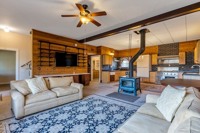 living room featuring a wood stove, ceiling fan, sink, and wood walls