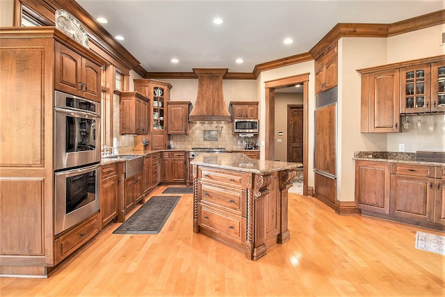 kitchen with custom exhaust hood, decorative backsplash, a kitchen island, appliances with stainless steel finishes, and light hardwood / wood-style floors