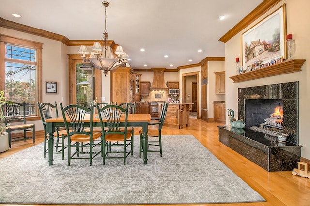 dining area featuring light hardwood / wood-style floors, a notable chandelier, crown molding, and a premium fireplace