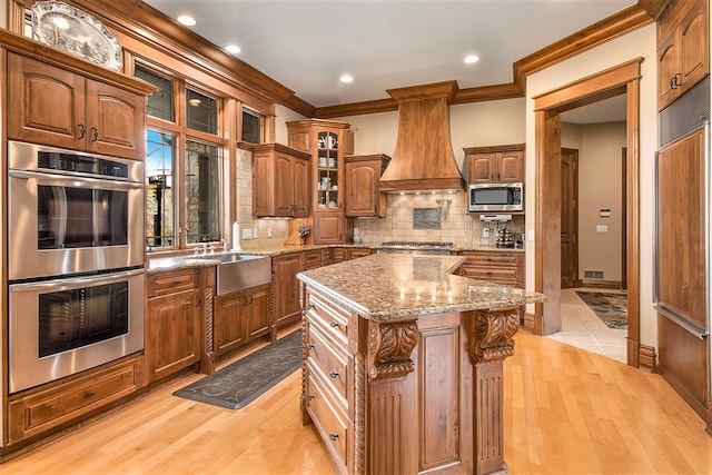 kitchen with light wood-type flooring, appliances with stainless steel finishes, a center island, and custom range hood