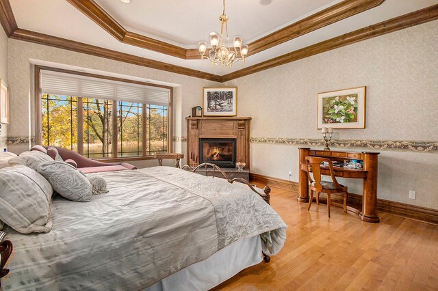 bedroom featuring a chandelier, a raised ceiling, ornamental molding, and light hardwood / wood-style flooring