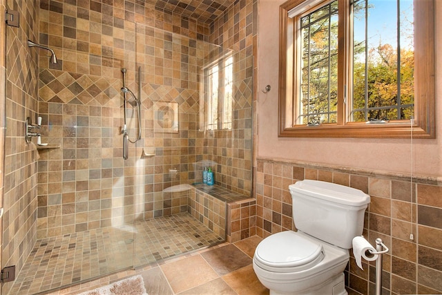 bathroom with a shower with door, tile walls, and toilet