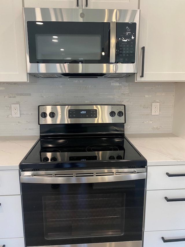 kitchen with light stone counters, white cabinetry, backsplash, and appliances with stainless steel finishes