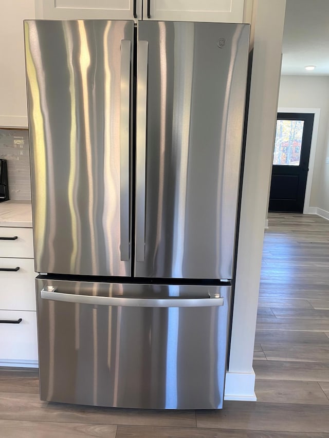 details with hardwood / wood-style flooring, decorative backsplash, stainless steel fridge, and white cabinetry