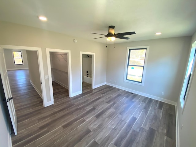 unfurnished bedroom with ceiling fan, a closet, dark wood-type flooring, and a spacious closet