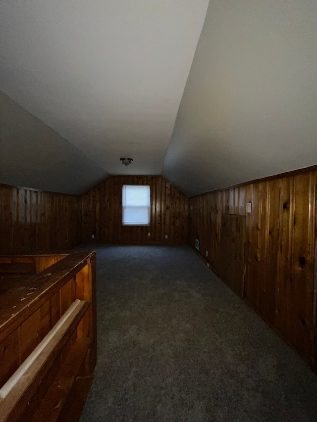 bonus room featuring dark carpet, vaulted ceiling, and wood walls