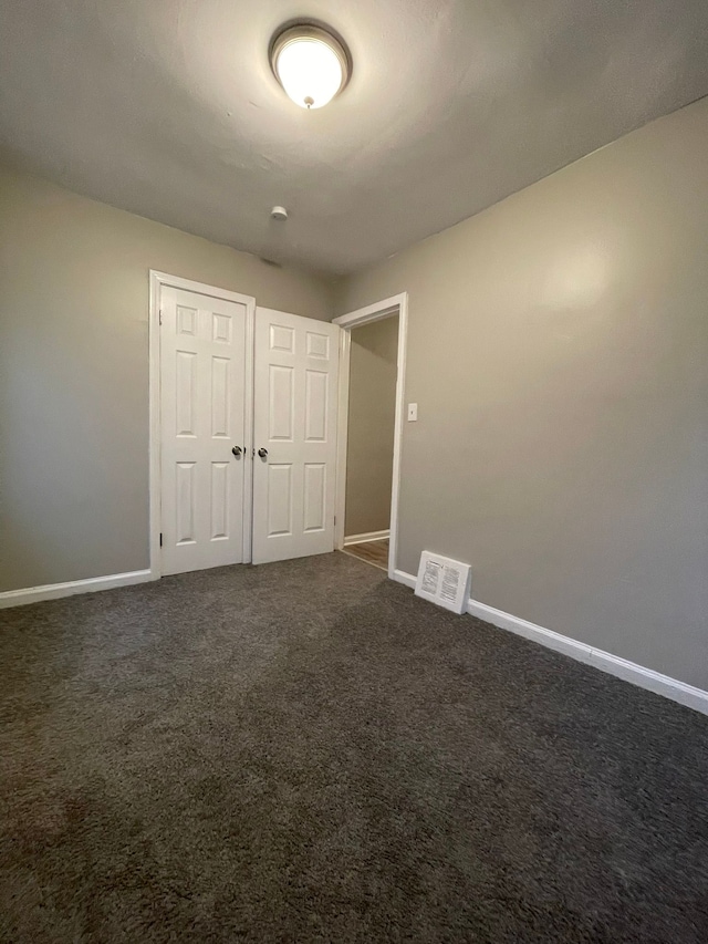 unfurnished bedroom with dark colored carpet and a closet