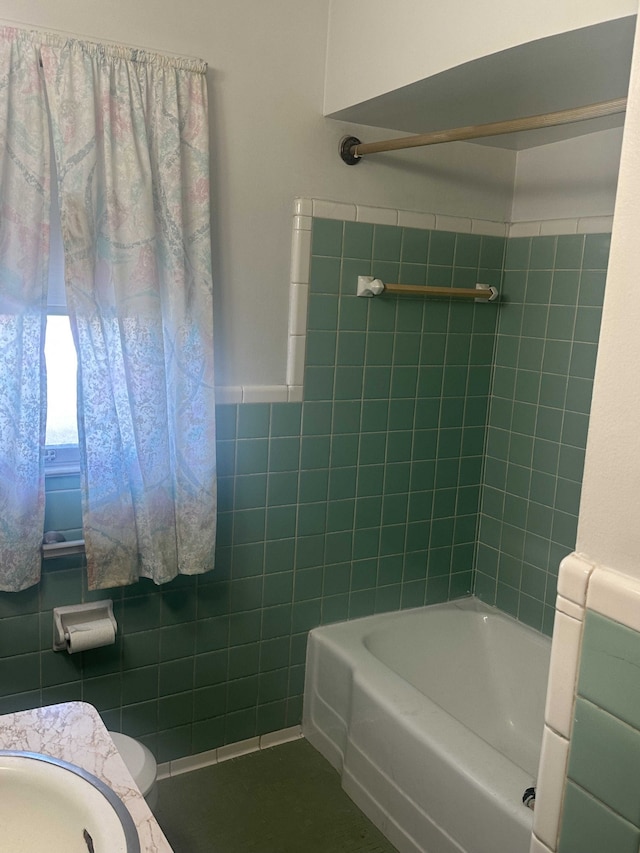 full bathroom with sink, tiled shower / bath combo, toilet, and tile walls