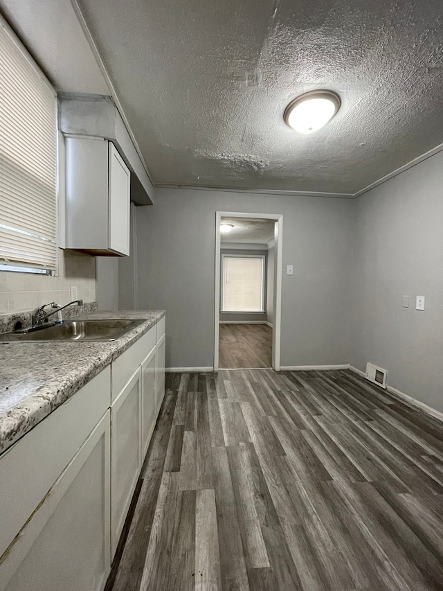 kitchen with a textured ceiling, dark hardwood / wood-style flooring, white cabinetry, and sink