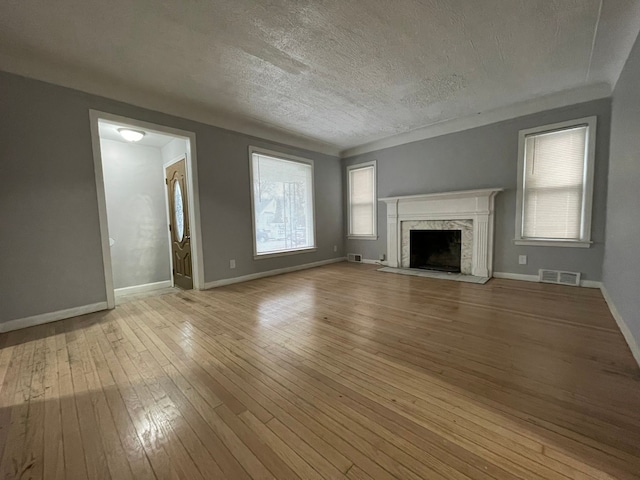 unfurnished living room with a high end fireplace, a textured ceiling, light hardwood / wood-style floors, and a wealth of natural light