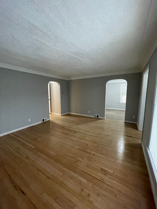 empty room with plenty of natural light, wood-type flooring, and a textured ceiling