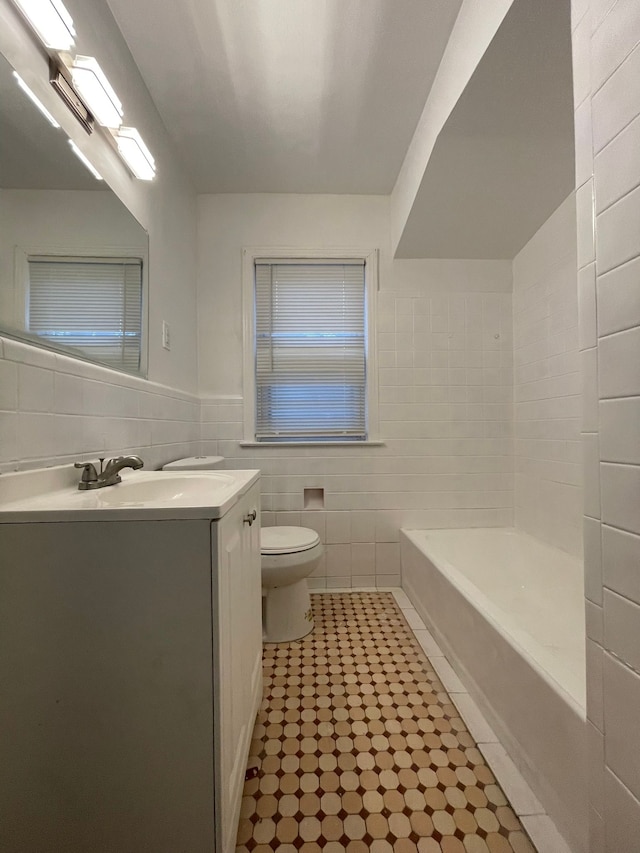 bathroom with vanity, toilet, tile walls, and a washtub