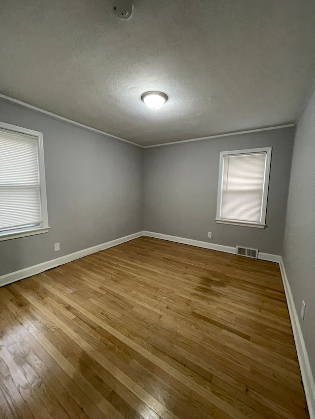 empty room with light wood-type flooring, a textured ceiling, and ornamental molding