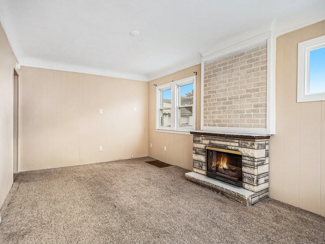 unfurnished living room with carpet flooring, a stone fireplace, and crown molding