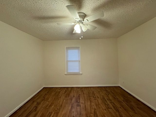 empty room featuring a textured ceiling, dark wood-type flooring, and ceiling fan