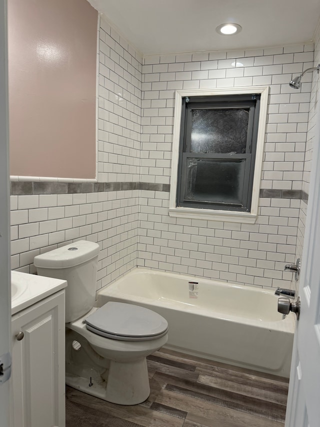 full bathroom featuring toilet, tiled shower / bath, tile walls, vanity, and hardwood / wood-style floors