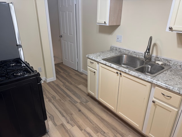 kitchen featuring black gas range oven, sink, light hardwood / wood-style flooring, cream cabinets, and light stone countertops