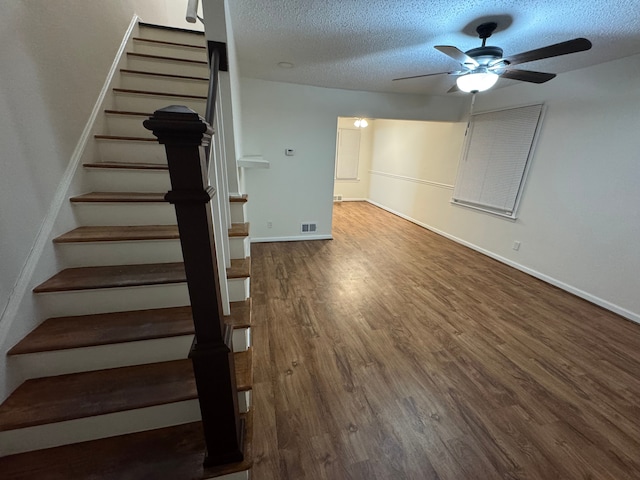 staircase featuring hardwood / wood-style flooring, ceiling fan, and a textured ceiling