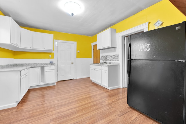 kitchen with decorative backsplash, light wood-type flooring, black fridge, sink, and white cabinetry