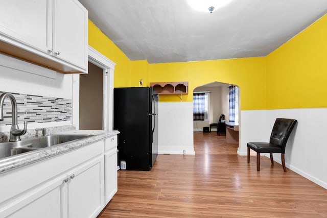 kitchen featuring black fridge, white cabinetry, sink, and light hardwood / wood-style flooring