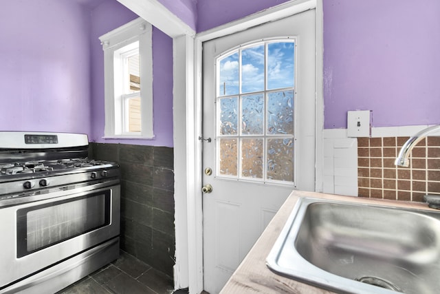 kitchen with stainless steel range with gas cooktop, sink, and tile walls