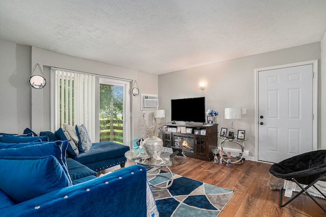 living room with a textured ceiling, a fireplace, hardwood / wood-style floors, and a wall mounted air conditioner