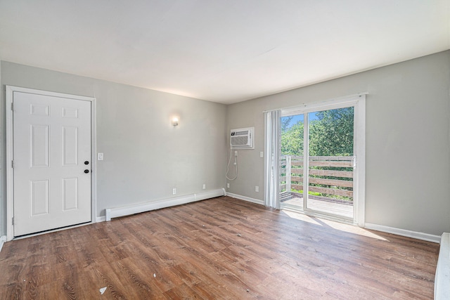 unfurnished room with an AC wall unit, a baseboard heating unit, and hardwood / wood-style flooring