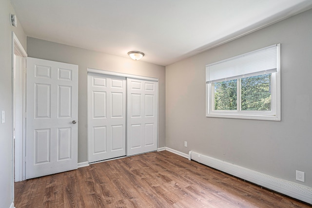 unfurnished bedroom featuring wood-type flooring, a closet, and baseboard heating