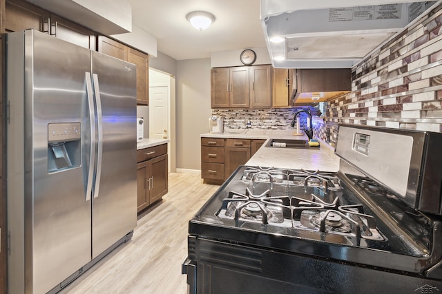 kitchen with sink, stainless steel appliances, tasteful backsplash, extractor fan, and light hardwood / wood-style floors