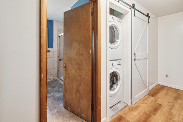 washroom featuring a barn door, stacked washing maching and dryer, and light hardwood / wood-style floors