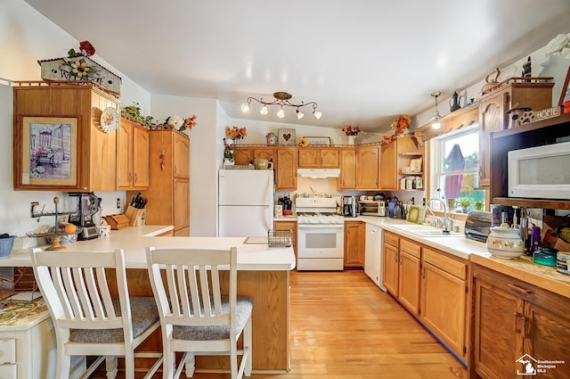 kitchen featuring sink, light hardwood / wood-style flooring, kitchen peninsula, white appliances, and a breakfast bar area