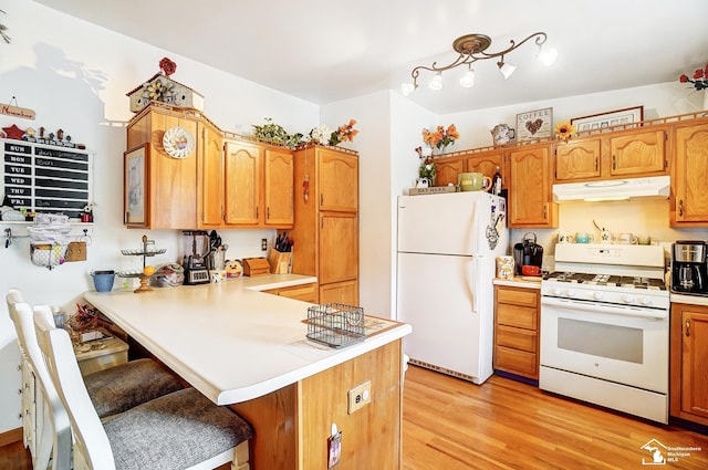 kitchen with a kitchen breakfast bar, light wood-type flooring, white appliances, and kitchen peninsula