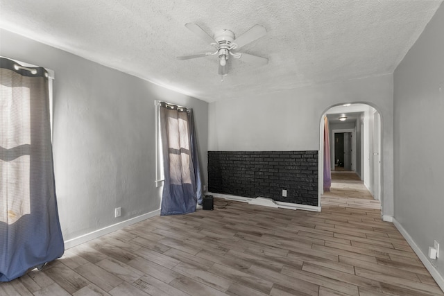 empty room with ceiling fan, light wood-type flooring, and a textured ceiling