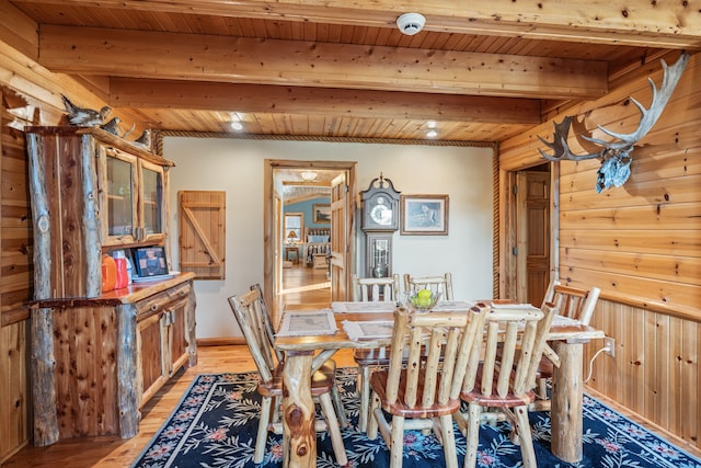 dining space featuring beamed ceiling, light wood-type flooring, wooden walls, and wooden ceiling