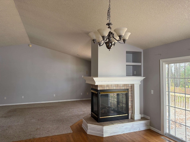 unfurnished living room featuring hardwood / wood-style floors, lofted ceiling, a fireplace, a textured ceiling, and a notable chandelier