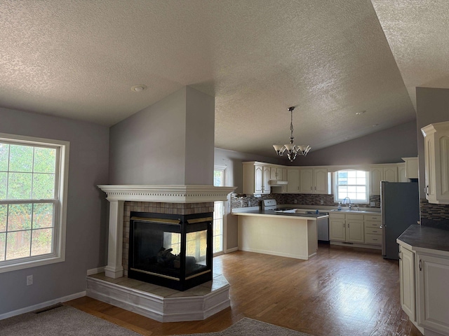 kitchen with kitchen peninsula, stainless steel fridge, wood-type flooring, lofted ceiling, and electric stove