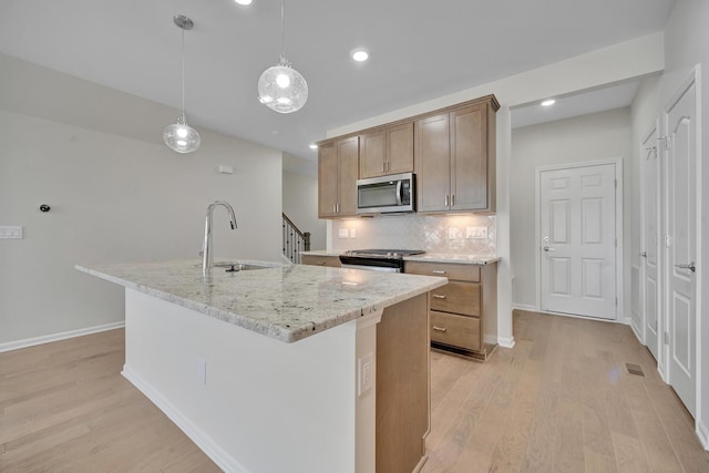 kitchen with stainless steel appliances, light wood-style flooring, a sink, tasteful backsplash, and an island with sink